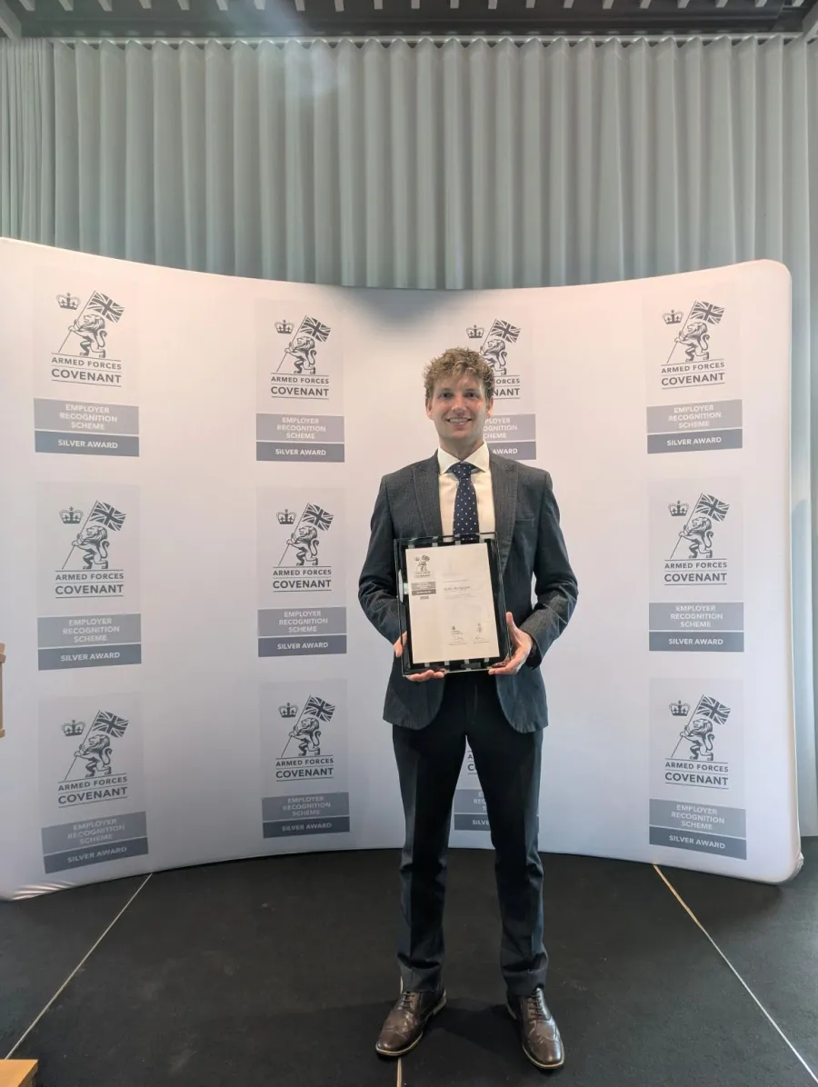 Henry Wright holding the framed Armed Forces Covenant Silver Award certificate in front of an Employer Recognition Scheme backdrop